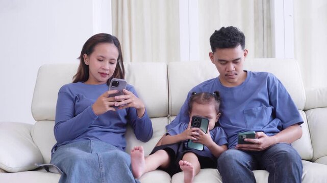 Asian Family Sitting on Sofa and Ignoring Each Other While Using Smartphones