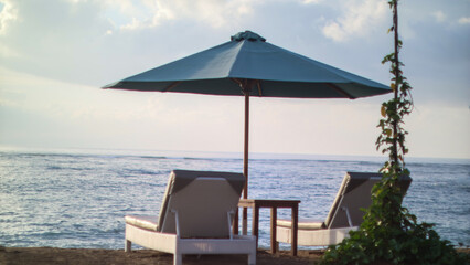 Relaxing beach chairs and teal parasol overlooking the calm ocean waves during a peaceful tropical sunset. © Ipramana