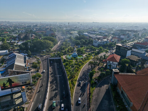 Aerial view of Patung Titi Banda monument surrounded by lush greenery and urban roads in Kecamatan Denpasar Timur, Bali, Indonesia.