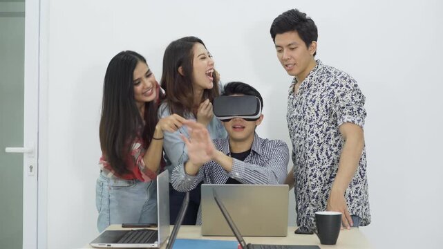 Group of Young Asian Friends Testing Virtual Reality VR Headset Together at Office Desk