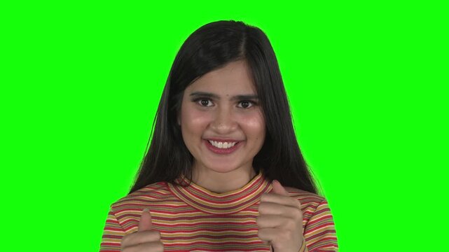 Young Asian woman showing angry expression and screaming before shifting to a happy smile with two thumbs up on green screen.