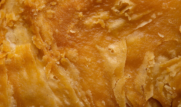Close-up texture of golden crispy puff pastry,Macro shot focusing on the detailed, flaky, and crispy layers of a freshly baked golden-brown curry puff pastry.