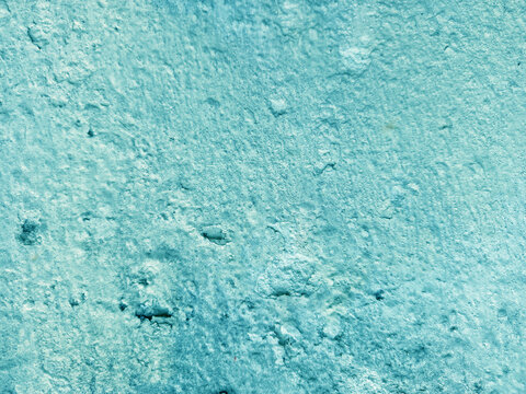 A close-up shot captures the rough, weathered texture of an old concrete wall. The surface is uneven, dark patches, mineral stains, and reflecting natural aging