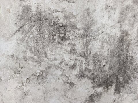 A close-up shot captures the rough, weathered texture of an old concrete wall. The surface is uneven, dark patches, mineral stains, and reflecting natural aging