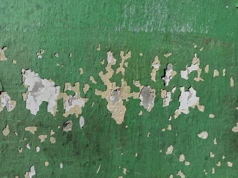 The rough, weathered texture of an old concrete wall. Its surface is uneven, featuring dark patches and mineral stains that reflect the natural aging process, along with peeling paint.