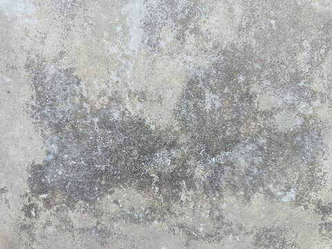 A close-up shot captures the rough, weathered texture of an old concrete wall. The surface is uneven, dark patches, mineral stains, and reflecting natural aging