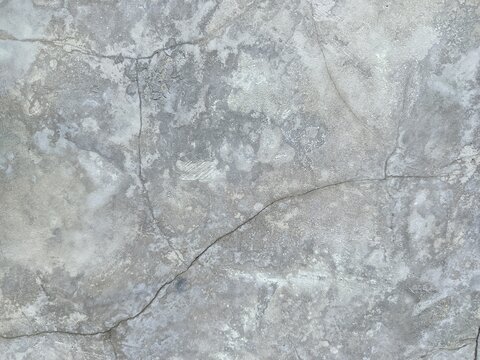 A close-up shot captures the rough, weathered texture of an old concrete wall. The surface is uneven, dark patches, mineral stains, and reflecting natural aging