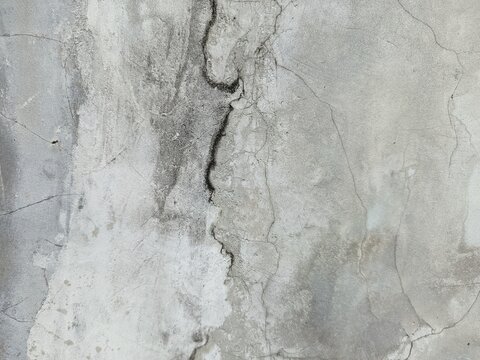 A close-up shot captures the rough, weathered texture of an old concrete wall. The surface is uneven, dark patches, mineral stains, and reflecting natural aging