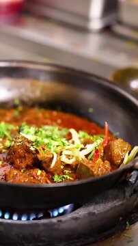 Chef Garnishing Spicy Meat Curry Simmering in Pan on Gas Stove