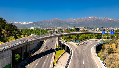 Fototapeta premium Modern highway interchange with traffic and the snow-capped Andes mountains in Santiago, Chile.