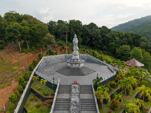Aerial view of the Goddess Kwan Im Statue standing on a stone platform surrounded by lush green trees and stairs in Damar, Bangka Belitung Island, Indonesia.