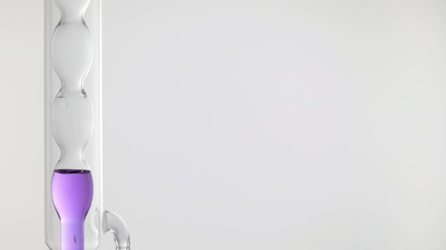 Close-up of pale clear violet liquid filling up vertically mounted bulb lab condenser on the left side of the frame, right side for copy space on grey | Cornflower hydrosol beauty ingredient concept