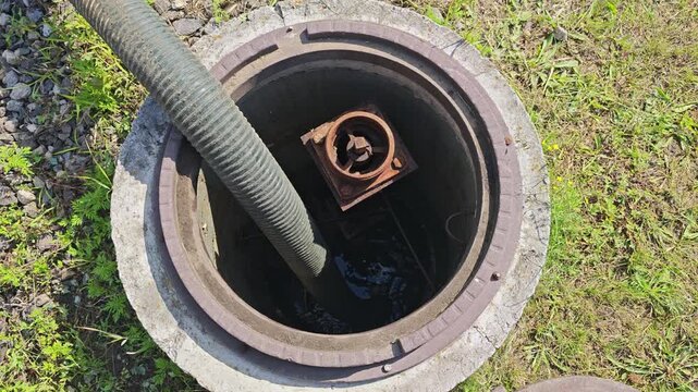 Top-down view of a suction hose pumping water out of an open concrete water supply manhole.