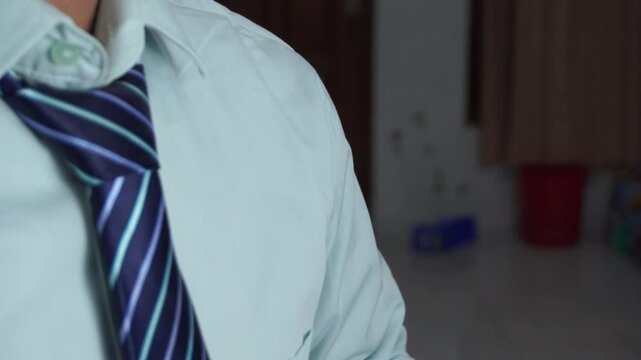 An Asian businessman looking in the dirty mirror while adjusting his blue striped necktie on a light green shirt. Professional man getting ready for a job interview or corporate work