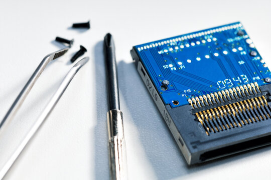 Computer chip, screwdriver, tweezer on desk, close-up. Electronics repair and maintenance concept.