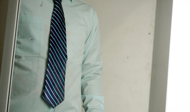 An Asian businessman looking in the dirty mirror while adjusting his blue striped necktie on a light green shirt. Professional man getting ready for a job interview or corporate work