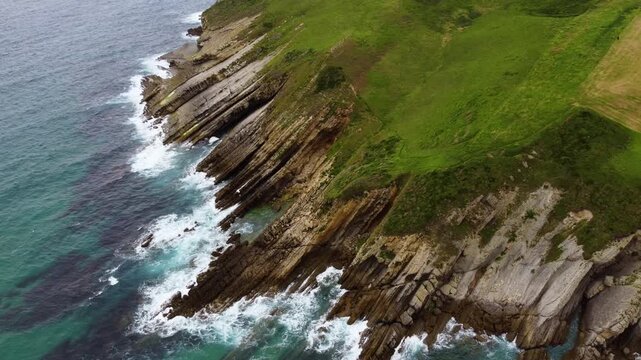 Dramatic aerial drone view of flysch rock formations and cliffs on the Cantabrian coast, Spain. Turquoise ocean waves crashing against unique geological strata. High quality 4k footage