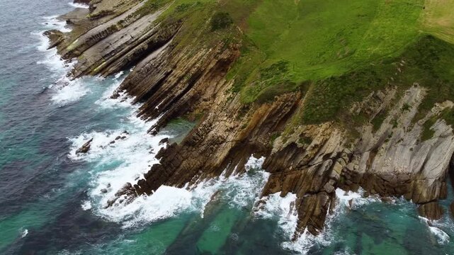 Dramatic aerial drone view of flysch rock formations and cliffs on the Cantabrian coast, Spain. Turquoise ocean waves crashing against unique geological strata. High quality 4k footage