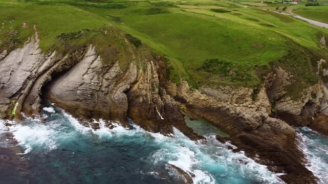 Dramatic aerial drone view of flysch rock formations and cliffs on the Cantabrian coast, Spain. Turquoise ocean waves crashing against unique geological strata. High quality 4k footage