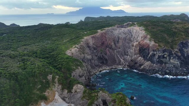 Aerial view of dramatic coves and rugged coastline on Shikinejima Island with distant Kozushima, Japan