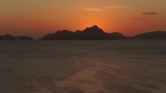 Aerial Sunset Descent Shot at Corong Corong Beach in El Nido. Drone Vertical Drop View Lowering Over Calm Ocean Facing Deep Orange Twilight Sky and Island Silhouettes.