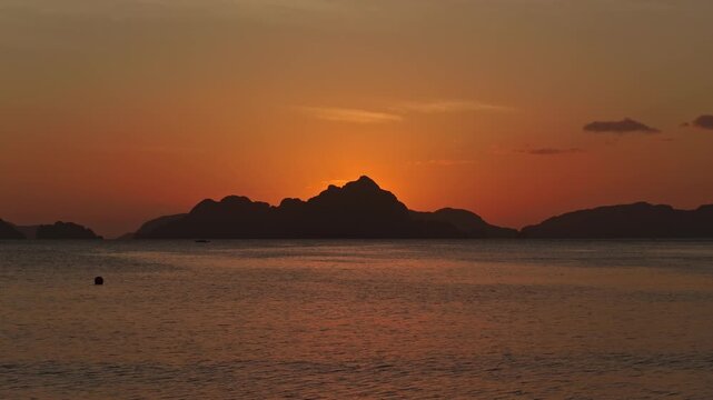 Low Altitude Aerial Forward Flight Towards Sunset at Corong Corong Beach, El Nido. Drone Cinematic Push In Over Calm Water Facing Deep Orange Twilight Sky and Islands.