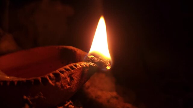 Traditional clay oil lamp diya burning with bright, steady flame in dark setting. Warm glow creates peaceful spiritual atmosphere, making it ideal for Diwali celebrations, Hindu worship, meditation