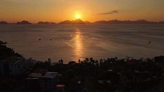 Aerial Sunset Panning Shot of Corong Corong Beach in El Nido, Philippines. Drone Left to Right Golden Hour View of Orange Sky and Sun Reflecting on Calm Ocean Water.