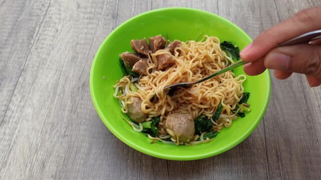 Close Up Of Delicious Mie Ayam With Meatballs And Greens Being Eaten With Spoon