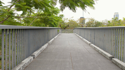 Fototapeta premium Modern Elevated Concrete Skywalk Through Lush Green Trees in Benchakitti Park