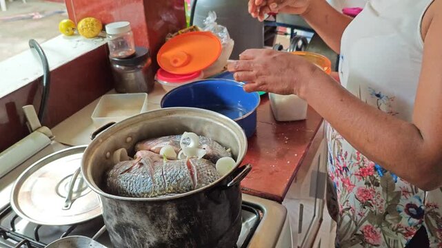 Woman adding sliced white onions into a pot with fresh tilapia fish
