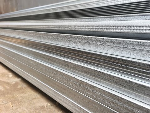 Stack of lightweight galvanized steel truss profiles for roof framing at a construction site, side view of stacked metal spandek or galvalume channels for residential house building