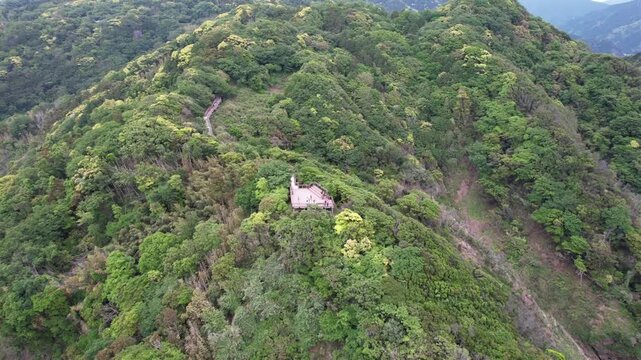 Aerial view of Lover's Cape in Izu Peninsular Japan reveals a small platform nestled within forested hills Green mountains roll gently toward a calm body of water. The structure stands alone, quiet, a