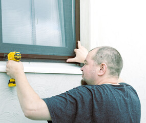 Fototapeta premium Man installs window screen with power drill