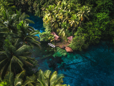 Aerial view of Danau Paisu Pok Luk Panenteng with clear blue water, lush palm trees, and a small wooden boat moored at a dock in Bulagi Utara, Central Sulawesi, Indonesia.