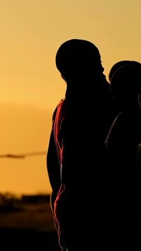 Vertical video: Entering right hooded boys forming line at sunset, practicing with ball, copy space