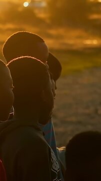 Vertical video: Soccer ball entering drawing boys in hoodie turning heads on dusty lot at sunset