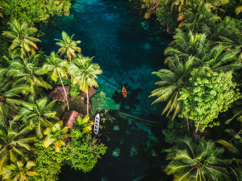 Aerial view of Danau Paisu Pok Luk Panenteng with turquoise water, lush palm trees, and a small boat floating on the surface in Bulagi Utara, Central Sulawesi, Indonesia.