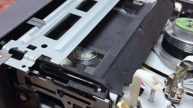 The internal gears and reels of a VCR rotate to play a VHS tape. This action creates a steady mechanical whirring sound combined with rhythmic clicks and the soft hiss of the spinning head.