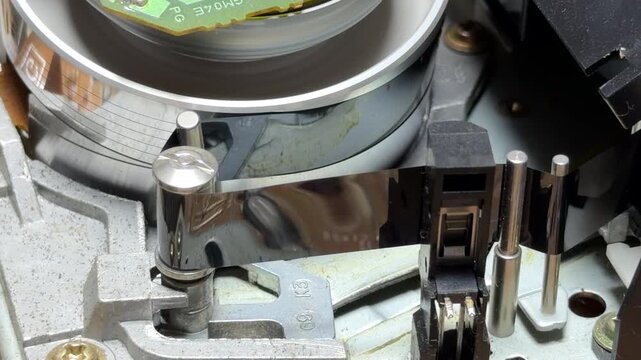 The internal gears and reels of a VCR rotate to play a VHS tape. This action creates a steady mechanical whirring sound combined with rhythmic clicks and the soft hiss of the spinning head.