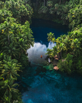 Aerial view of Danau Paisu Pok Luk Panenteng with a small boat on clear blue water surrounded by dense palm trees in Bulagi Utara, Central Sulawesi, Indonesia.