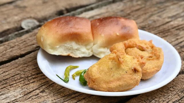 vada pav, mumbai famous vada paav is an indian burger. potato patty is deep fried and stuffed inside a paav or bun like burger, served over a rustic wooden background