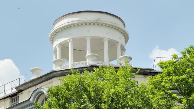 A majestic white rotunda stands tall above lush green trees in Simferopol, Crimea. The elegant architecture shines under a peaceful blue sky, bringing a serene feeling.