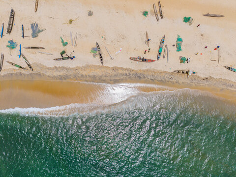 Aerial view of traditional wooden fishing boats resting on the sandy beach with fishermen and colorful nets scattered along the shoreline in Monrovia, Liberia.