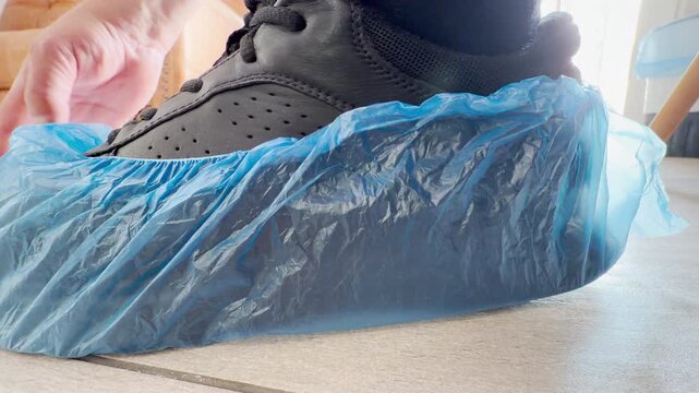 A person carefully pulls a blue protective shoe cover over a black sneaker on a clean indoor floor. This responsible action brings a reassuring sense of safety and cleanliness to the room.