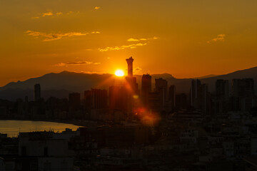 Fototapeta premium Dramatic sunset over the Benidorm skyline in Spain with the Intempo Building silhouetted against a glowing orange sky and distant mountains creating a striking cityscape above the Mediterranean coast