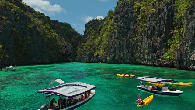 Low Altitude Aerial Flyover of Tour Operators and Kayakers at Small Lagoon in El Nido, Philippines. Drone Close Forward Tracking Shot Over Boats and Tourists on Turquoise Water.