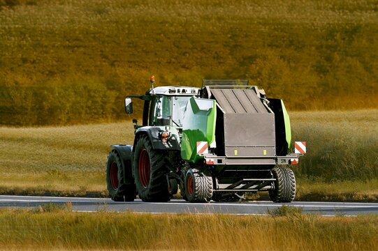 Tractor towing baler through peaceful countryside road