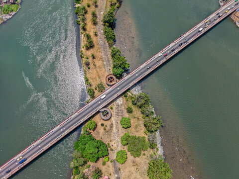 Aerial view of the Mesurado River Bridge with cars driving across the water, surrounded by lush green vegetation and riverbanks in Monrovia, Liberia.