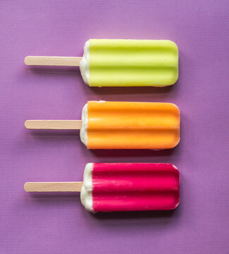 Three colorful ice pops lined up on a purple background